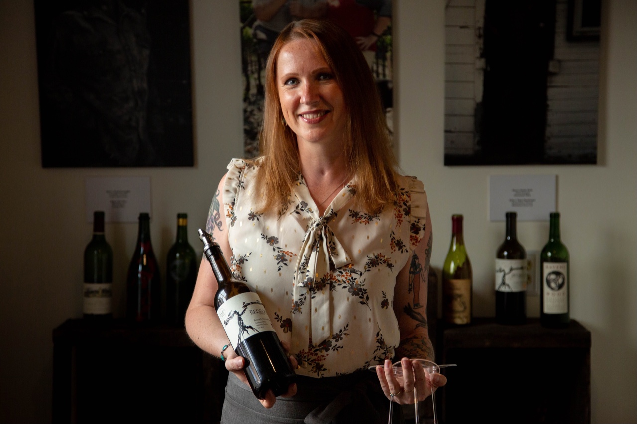 Aiste Nichols holding a bottle of wine and three glasses at the Bedrock tasting room